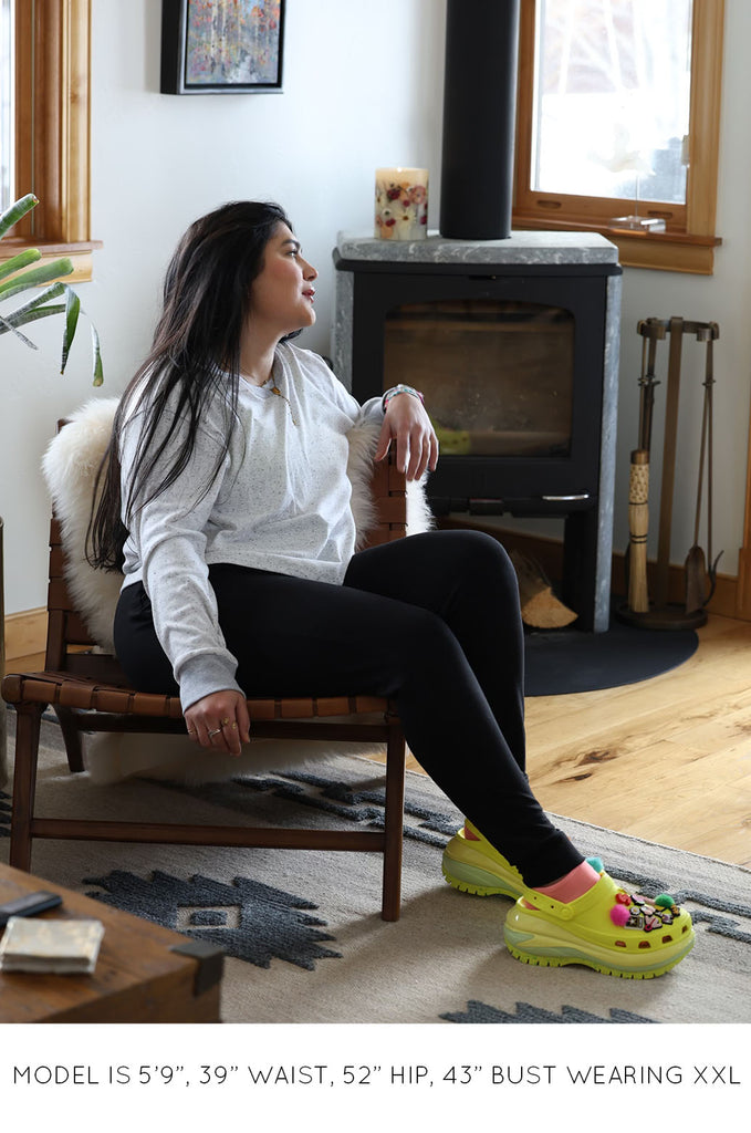 Model sitting down wearing black pants and grey long sleeve top by Miakoda. 