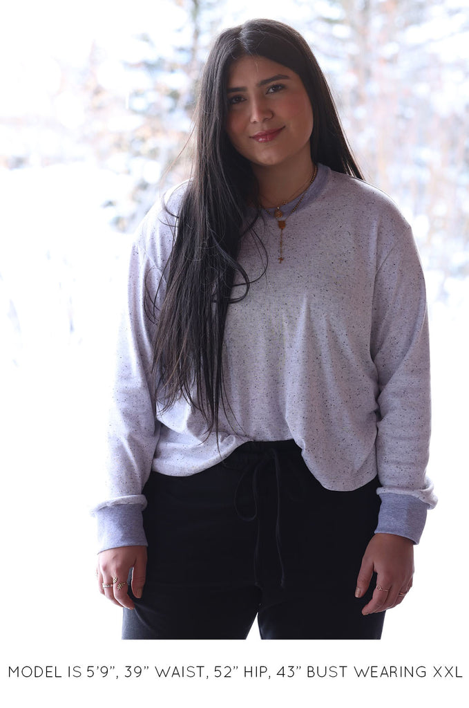 Model with snowy background wearing grey long sleeve top by Miakado. 
