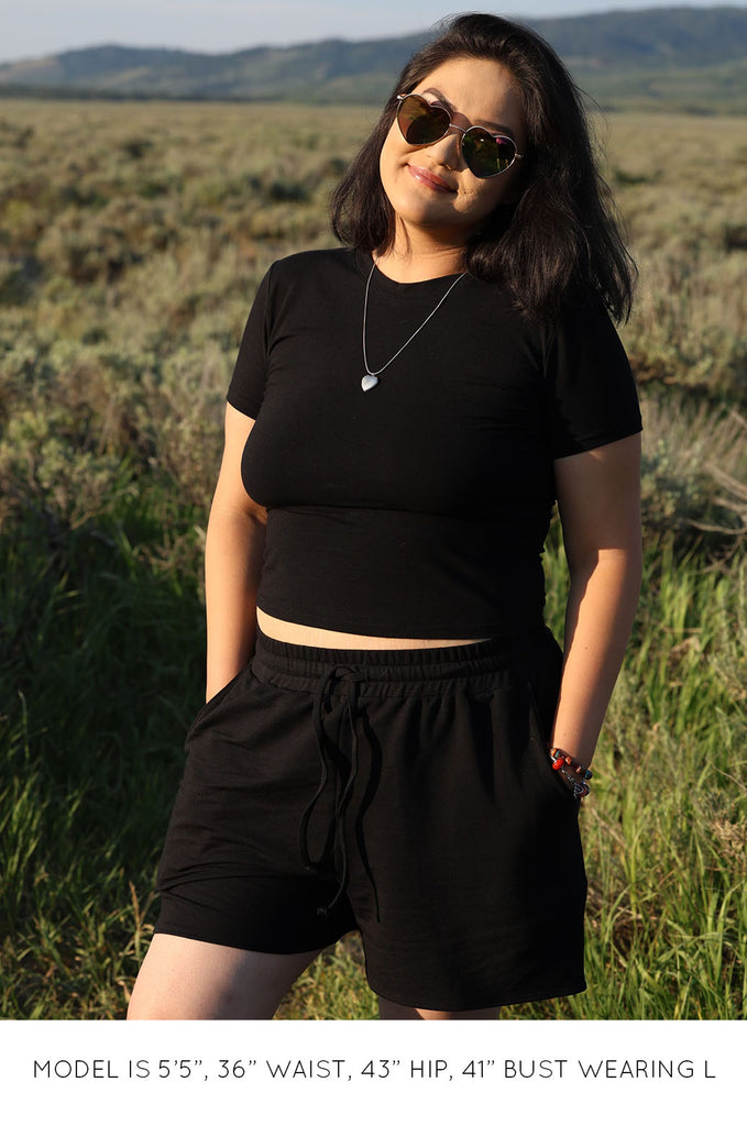 Woman in field wearing black Miakoda Baby Tee with black shorts. 