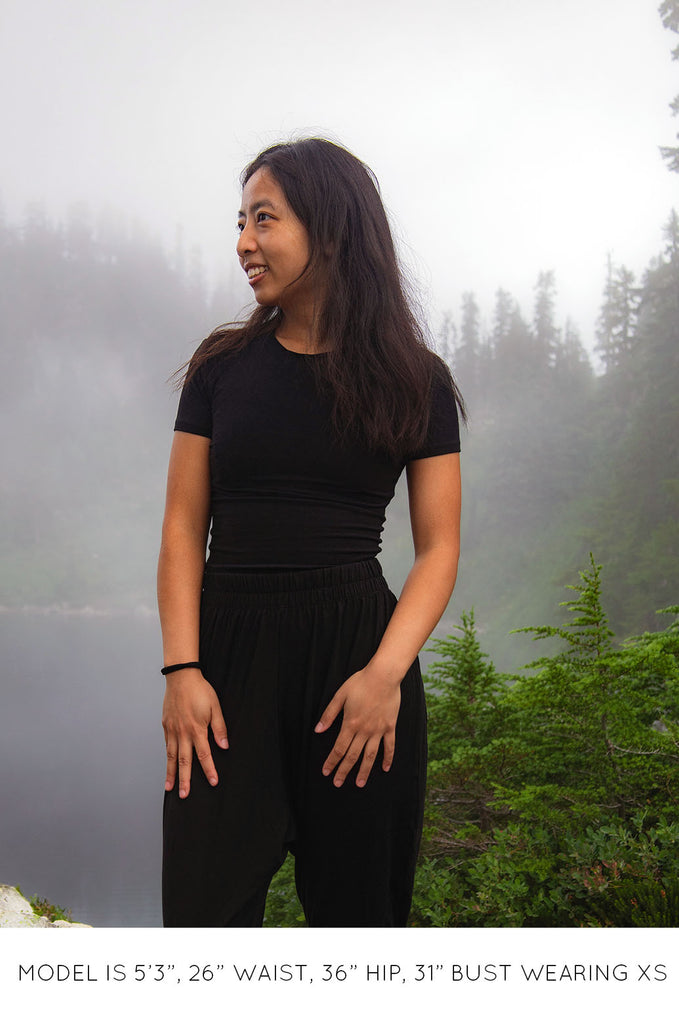 Model in misty forest wearing black Miakoda Baby Tee with black pants. 