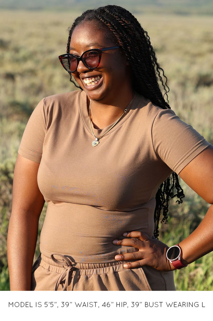 Model in field wearing brown Miakoda Baby Tee with matching shorts. 