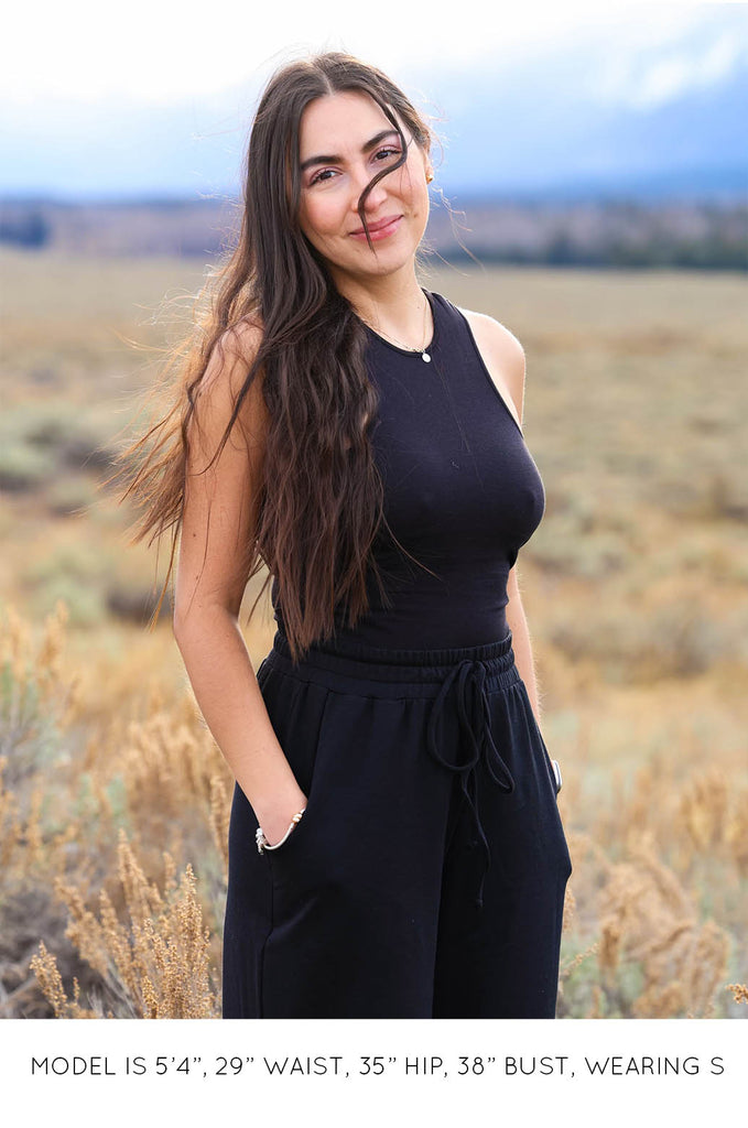 Model standing outside wearing black racer tank by Miakoda. 