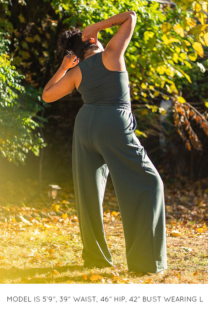 Back view of model in front of tree wearing green racer back tank and green wide leg pants by Miakoda. 