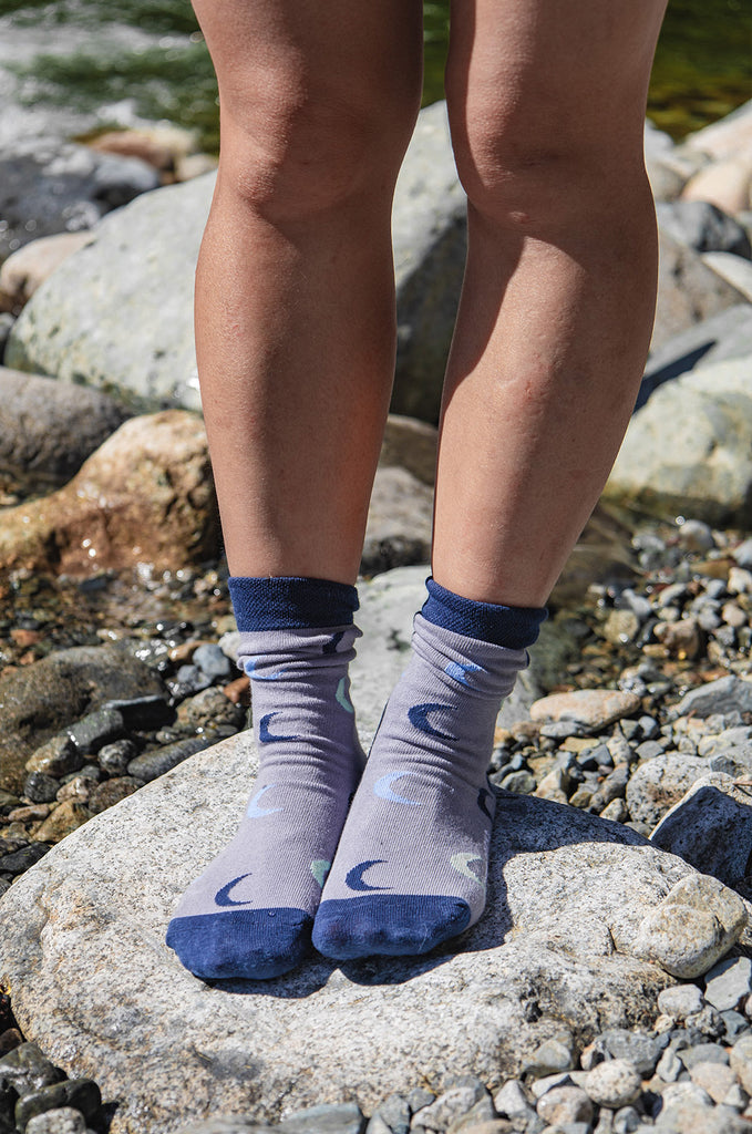 Woman standing on rock wearing grey and blue Miakoda unisex Moon socks. 
