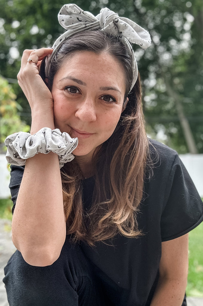 Woman wearing matching grey print headband and scrunchie by Miakoda. 